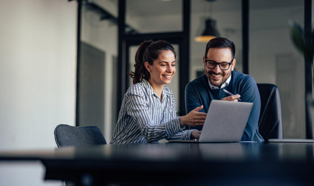 Hymyilevät ihmiset katsovat yhdessä tietokoneen ruutua